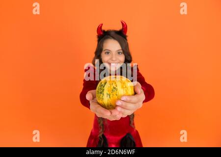 verdura di zucca nelle mani di felice diavolo capretto indossare corna costume di imp su festa di halloween, fuoco selettivo, cibo di halloween. Foto Stock