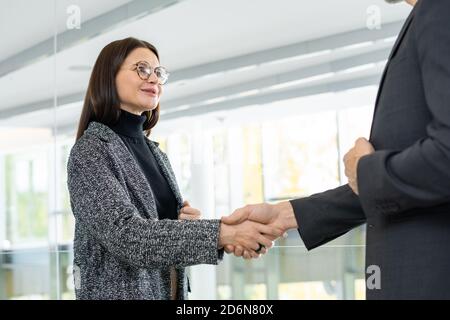 Giovane donna d'affari contemporanea di successo che scuote la mano del partner d'affari Foto Stock