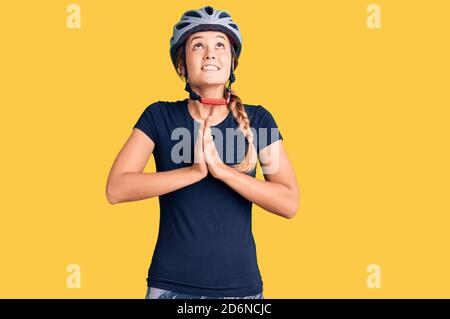 Bella donna caucasica che indossa casco da bici che prega con le mani insieme con espressione di speranza sul viso molto emotivo e preoccupato Foto Stock