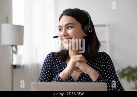Sorridente donna asiatica in cuffie distratto dal computer sognare Foto Stock
