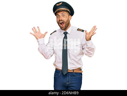 Bell'uomo con la barba che indossa l'uniforme pilota dell'aeroplano che celebra pazzo e stupito per il successo con le braccia sollevate e gli occhi aperti che gridano eccitato. winn Foto Stock