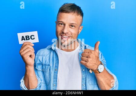 Bell'uomo muscolare tenendo lettere abc su carta sorridente felice e positivo, pollice su facendo eccellente e segno di approvazione Foto Stock