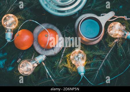 Picnic invernale con due arance e una tazza di tè in legno su rami di abete rosso decorati con ghirlande di Natale con luci. Vista dall'alto Foto Stock