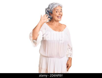 Donna anziana con capelli grigi che indossa una cintura in stile bohémien che dice ciao felice e sorridente, amichevole gesto di benvenuto Foto Stock