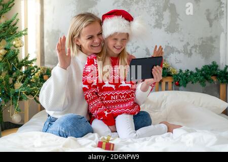 Natale online famiglia Complimenti. Sorridente madre bionda europea e figlia che usa un tablet mobile per videochiamare amici e genitori Foto Stock