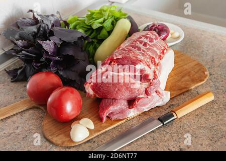 Carne cruda, un grosso pezzo di maiale fresco su una tagliere. Un pezzo di maiale con basilico, pomodoro e aglio è pronto per la cottura Foto Stock