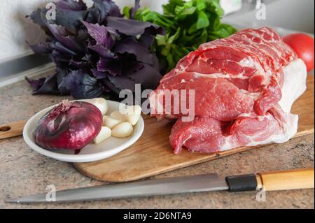 Carne cruda, un grosso pezzo di maiale fresco su una tagliere. Un pezzo di maiale con basilico, pomodoro e aglio è pronto per la cottura Foto Stock