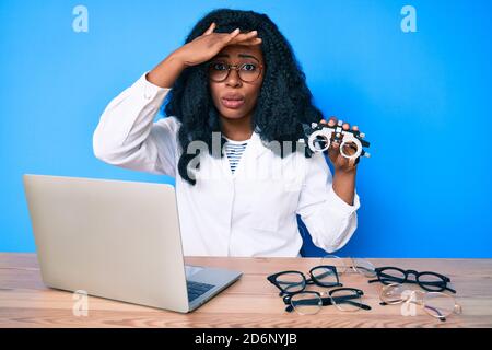 Bella donna africana che tiene occhiali di optometria stressati e frustrati con la mano sulla testa, sorpresa e faccia arrabbiata Foto Stock
