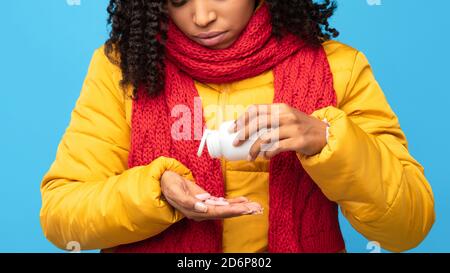 Malato Africano Signora che prende pillole che tiene bottiglia di medicina, sfondo blu Foto Stock