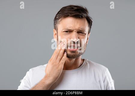 Uomo che soffre di forte dolore ai denti, fondo grigio Foto Stock