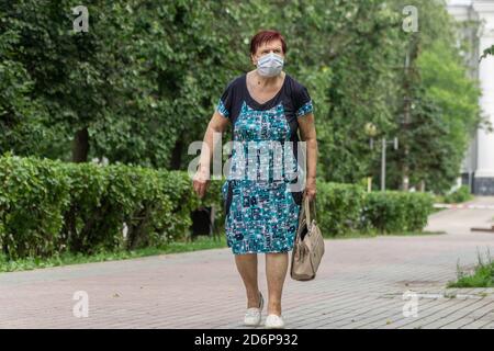 Donna anziana solitaria che indossa una maschera medica protettiva che cammina lungo la strada in città. La sopravvivenza degli anziani durante la pandemia. Foto Stock