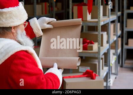 Babbo Natale che legge vuoto lista dei desideri nel magazzino dei regali dell'officina. Foto Stock