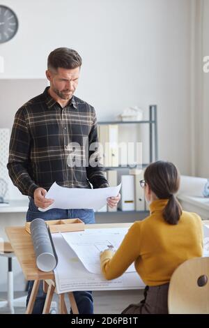Ritratto verticale di due architetti che discutono di progetti mentre lavorano insieme alla scrivania in ufficio Foto Stock