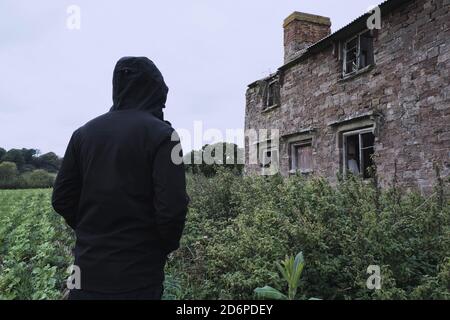 Guardando in su ad una casa abbandonata spooky, con una figura agganciata, di nuovo alla macchina fotografica. In campagna Foto Stock