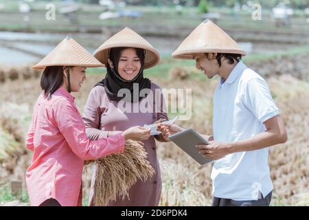 gruppo di coltivatori che indossano un cappello che tiene il raccolto e. tablet mentre si è in piedi nei campi Foto Stock