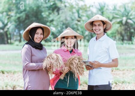 gruppo di coltivatori che indossano un cappello che tiene il raccolto e. tablet mentre si è in piedi nei campi Foto Stock