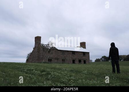 Guardando in su ad una casa abbandonata spooky, con una figura agganciata, di nuovo alla macchina fotografica. In campagna Foto Stock