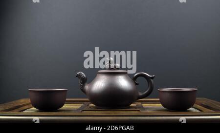 Un antico teapot e due ciotole in argilla su una superficie in legno con uno sfondo grigio Foto Stock