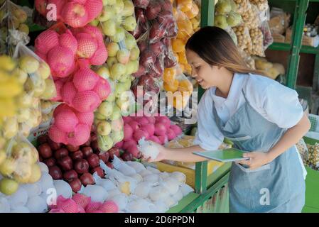 Felice proprietario di donna che usa il tablet digitale nel negozio di frutta quando prendere appunti Foto Stock