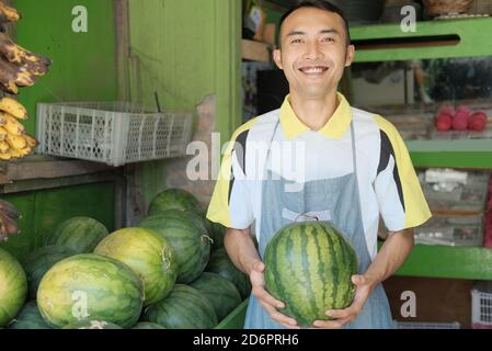 Negozio cameriera ragazzo in grembiule portare cocomero al basamento della frutta, concetto di frutta fresca Foto Stock