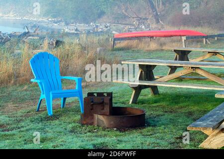 Una sedia blu accanto a una fossa dei vigili del fuoco allo Spencer Spit state Park sull'isola di Lopez, Washington, USA Foto Stock