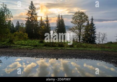 Riflessione nuvola nelle pozzanghere sulla strada di montagna. Tempo autunnale Foto Stock