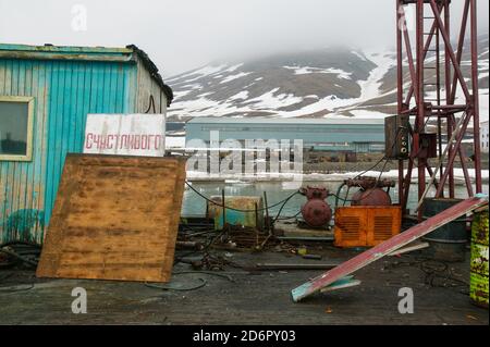 Vecchia casa e macchinari al porto della città artica Pyramiden a Svalbard, Norvegia. Pyramiden è un insediamento abbandonato di miniere di carbone a Svalbard. La piccola città artica fu abbandonata nel 1998. Foto Stock