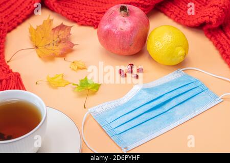 Foglie d'acero, melograno, limone, tazza da tè, maschera medica, sciarpa rossa, mockup su sfondo arancione. Concetto, autunno, vitamine per la salute, quarantena a causa del coronavirus. Foto di alta qualità Foto Stock