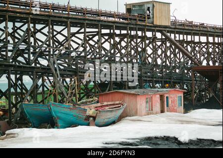 Barche e vecchia casa vicino al porto nella città artica Pyramiden a Svalbard, Norvegia. Pyramiden è un insediamento abbandonato di miniere di carbone a Svalbard. La piccola città artica fu abbandonata nel 1998. Foto Stock