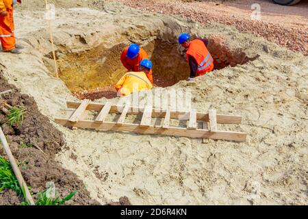 I lavoratori utilizzano pale per impostare le fondamenta su misura corretta in trincea quadrata, scale di legno poste a terra vicino. Foto Stock