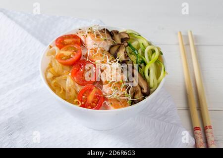ciotola di tagliatelle cinesi con funghi di shitake di salmone cipolla zucchina e pomodoro su tavola di legno bianco Foto Stock