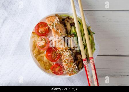 ciotola di tagliatelle cinesi con funghi di shitake di salmone cipolla zucchina e pomodoro su tavola di legno bianco Foto Stock