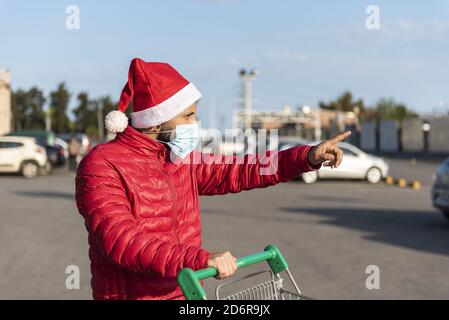 Uomo in una maschera medica con un cappello Babbo Natale con un carrello Foto Stock