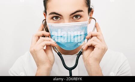 Ritratto di un medico esperto che indossa una maschera protettiva e uno stetoscopio alle orecchie mentre lavora in ospedale. Pandemia, covidio, protezione da virus Foto Stock