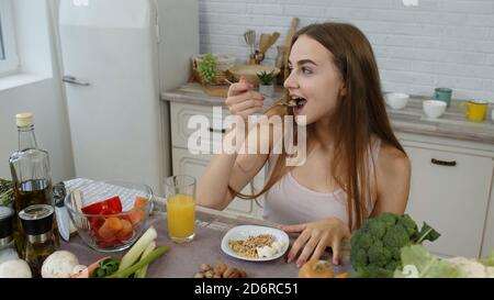 Bella ragazza con capelli lunghi mangiare germogli crudi grano saraceno con noci in cucina con verdure fresche e frutta. Sano biologico eco cibo vegetariano concetto. Perdita di peso e stile di vita dietetico Foto Stock