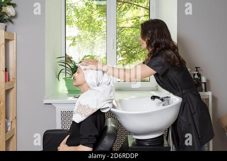 carino parrucchieri pulisce i capelli del cliente con un asciugamano. giovane donna ottiene un lavaggio della testa al barbiere Foto Stock