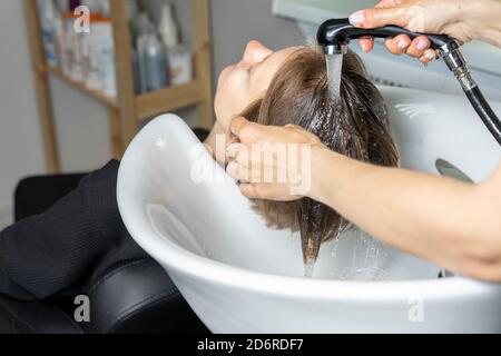 le mani del parrucchiere lavano i capelli della giovane donna nel salone di bellezza Foto Stock