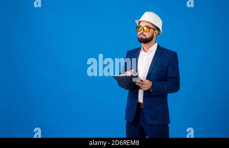 Un giovane professionista che indossa un elmetto e che porta un appunti su sfondo blu Foto Stock