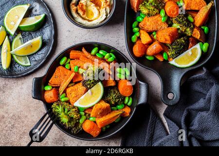 Verdure cotte in padelle di ghisa, sfondo scuro. Patate dolci al forno, broccoli, carote e fagioli. Foto Stock