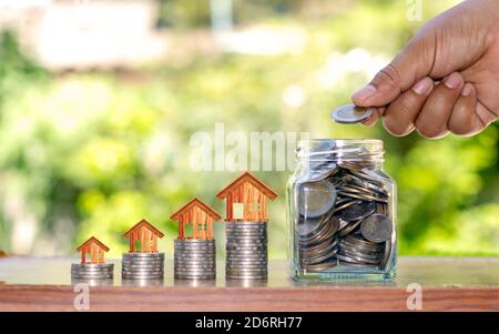 Le mani dell'uomo che tiene il denaro in una bottiglia per risparmiare denaro, tra cui una casa in cima alla moneta, denaro risparmio idee per l'acquisto di una casa. Foto Stock