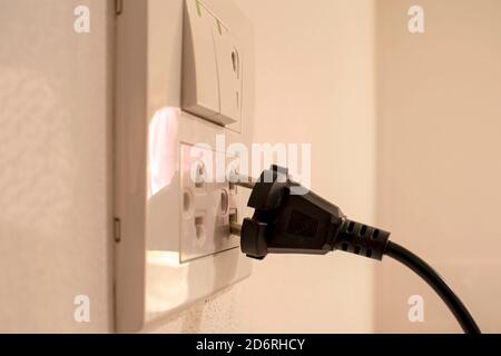 I pericoli derivanti dall'uso di elettricità a casa o in ufficio, comprese le mani nere che non sono completamente collegate alla parete bianca. Foto Stock