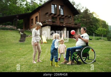 Bambini piccoli con nonni anziani in sedia a rotelle che giocano con una palla in giardino. Foto Stock