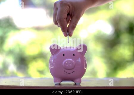 Primo piano di una donna che mette una moneta in una banca piggy. Concetto di risparmio di denaro. Foto Stock