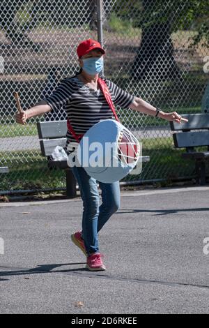 Un membro asiatico americano di un ensemble di batteria prova in un parco in Queens, New York City mentre indossa una maschera chirurgica. Foto Stock