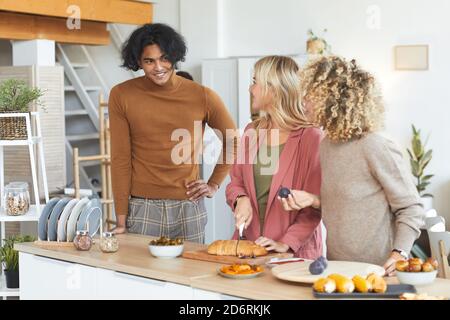 Vita in su ritratto di tre amici che chiacchierano felicemente mentre cucinano per la festa della cena all'interno, spazio di copia Foto Stock