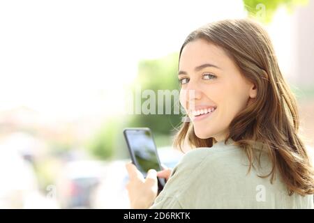 Donna felice che usa il telefono cellulare sorridendo alla fotocamera nel via Foto Stock