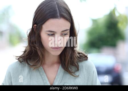 Vista frontale ritratto di una donna triste che si lamenta guardando giù camminando per strada Foto Stock