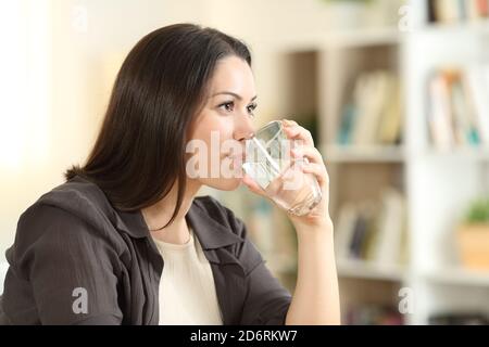 Donna che beve acqua dal vetro guardando lontano a casa Foto Stock