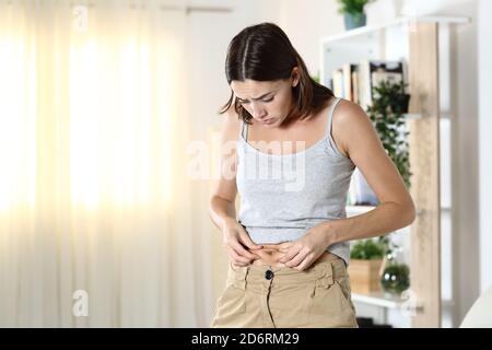 Donna preoccupata per il grasso del corpo che tocca la sua pancia in piedi a. casa Foto Stock