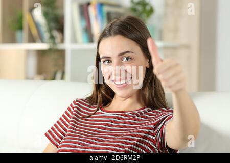 Donna felice sorridente alla macchina fotografica con il pollice su seduto un divano nel soggiorno di casa Foto Stock
